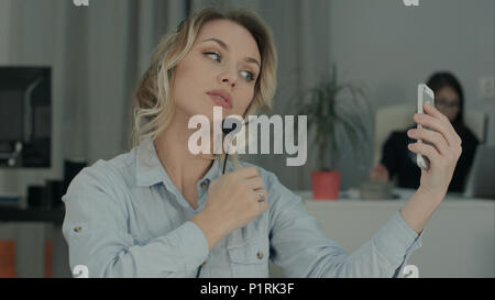 Young office worker in headset taking selfies on her phone Stock Photo