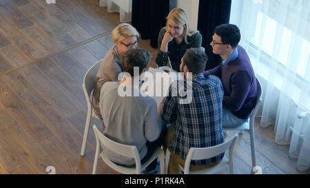 Team communication, group of five people discussing something with smile while sitting at the office table Stock Photo