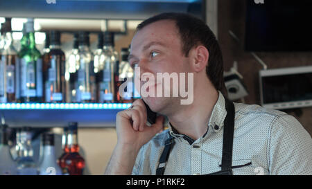 Happy barman in apron calling on smartphone at bar Stock Photo