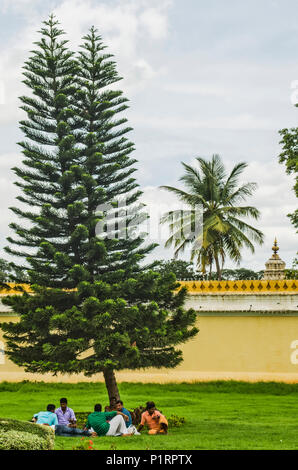 Men resting underneath a pine tree, Mysore Palace; Mysore, Karnataka, India Stock Photo