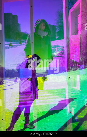 A woman takes a photo of her friend through the neon plexiglass of a Warming Hut Art Structure along the Red River Mutual Trail Stock Photo