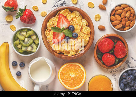 Healthy breakfast - bowl of corn flakes, berries and fruit, nuts, orange juice, milk, top view. Stock Photo