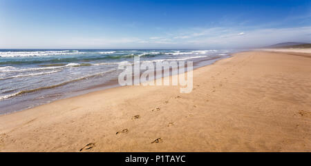 Water lapping on long sandy beach on hot summers day with foorprints leading into the distance Stock Photo
