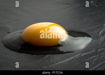 Broken Raw Egg Yolk on Dark Stone Background Stock Photo