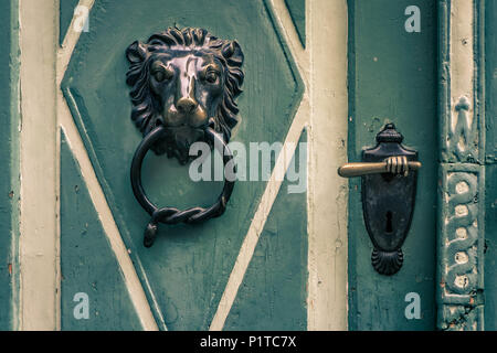 Ornate bronze door knocker and handle of an old, green and white wooden door. Stock Photo