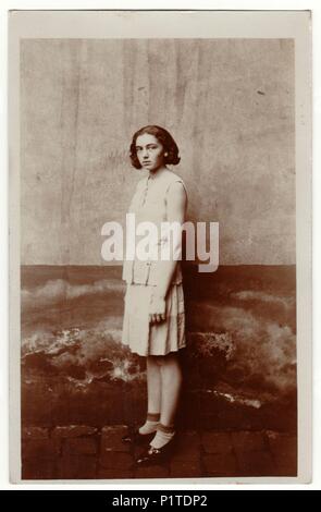 PRAGUE, THE CZECHOSLOVAK REPUBLIC - CIRCA 1940s: Vintage photo shows young girl stands outside. She wears a light dress. Retro black & white photography. Stock Photo