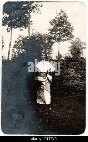 THE CZECHOSLOVAK REPUBLIC - CIRCA 1930s: Vintage photo shows woman wears white dress and she holds ladies hat (cloche hat). The woman poses outdoors. Retro black & white photography. Stock Photo