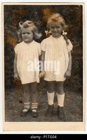 GERMANY - DECEMBER 23, 1946: Vintage photo shows two small girls (siblings). They wear a white dresses. Retro black & white photography. Stock Photo