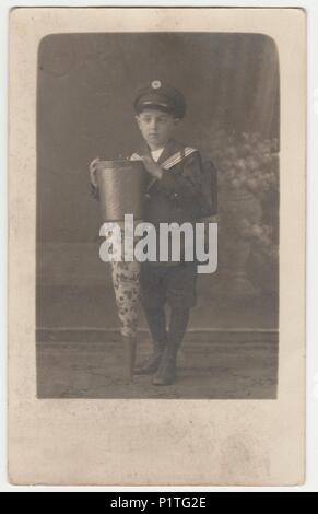 WALDENBURG, GERMANY - CIRCA 1920s: Vintage photo shows little boy with a School Cone ('Tute'), a big cardboard cone with toys, chocolate, candies, given the first day of school. Retro black & white studio photography. Stock Photo