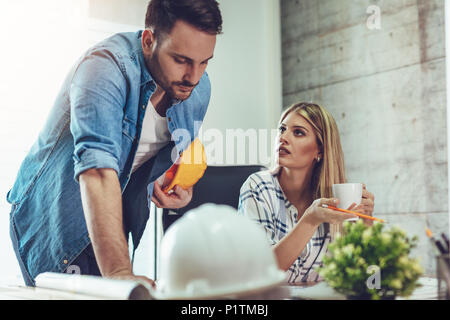 Young worried architect colleagues talking and analyzing blueprints while working on a new project at the office. Stock Photo