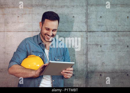 Young handsome successful entrepreneur looking on his tablet, checking plans before starting to work on construction site. Stock Photo