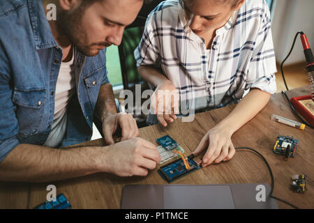 Man is helping woman soldering elements of circuit board. Stock Photo