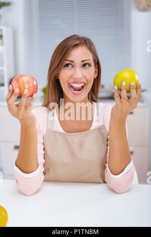 Adorable young woman with cheerful expression, holds two fresh apples, demonstrates her breakfast, Stock Photo