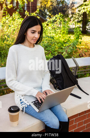 A young female university student  of Lebanese ethnicity sitting on a bench using her laptop in a quiet place on campus; Edmonton, Alberta, Canada Stock Photo