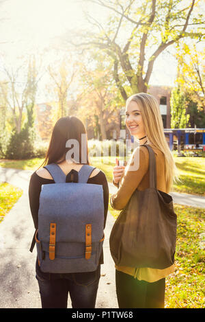 Two female student friends walk together on a university campus, one young woman glancing back towards the camera; Edmonton, Alberta, Canada Stock Photo