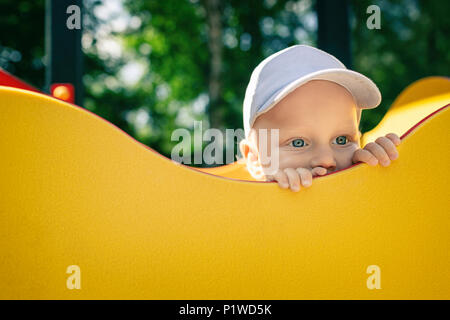 Baby boy playing in playground alone. Portrait of toddler looking away with unhappy face. Holding a toy on playground area outdoors. Stock Photo