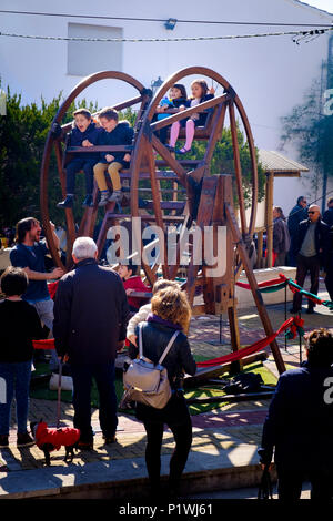 Young children enjoying on a traditional man driven small ferris wheel at a Spanish village Fiesta. Stock Photo