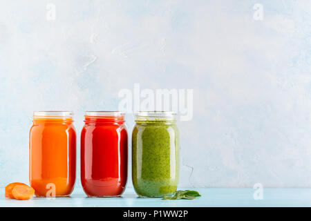 Orange/green/red colored smoothies / juice in a jar on a blue background. Stock Photo