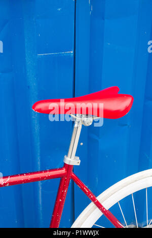Bright red saddle of a bike against bright blue background of container Stock Photo