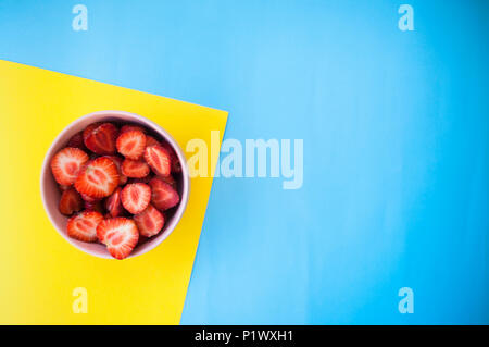 A pink bowl full of beautiful fresh juicy strawberries on bright yellow and blue background with text space.