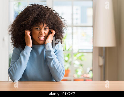 African american woman at home covering ears with fingers with annoyed expression for the noise of loud music. Deaf concept. Stock Photo
