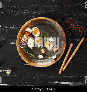 Bruschetta with cream cheese, fried eggs, mushrooms and salad leaves lying on plate standing on blue aged wooden surface with quail eggs and bread sti Stock Photo