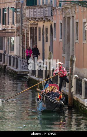 Venice, Italy - March 23, 2018: Venetian gondolier riding tourists on gondola through the side narrow canal in Venice. Stock Photo