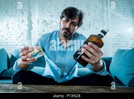 drunk alcoholic lain business man drinking whiskey from the bottle and glass depressed wasted and sad at home couch in alcohol abuse and alcoholism co Stock Photo