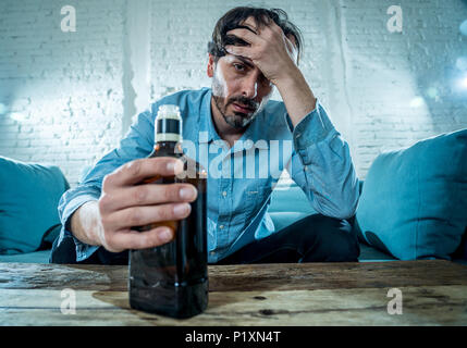 drunk alcoholic lain business man drinking whiskey from the bottle and glass depressed wasted and sad at home couch in alcohol abuse and alcoholism co Stock Photo