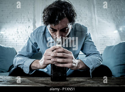 drunk alcoholic lain business man drinking whiskey from the bottle and glass depressed wasted and sad at home couch in alcohol abuse and alcoholism co Stock Photo