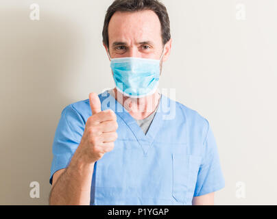 Senior doctor man using mask happy with big smile doing ok sign, thumb up with fingers, excellent sign Stock Photo