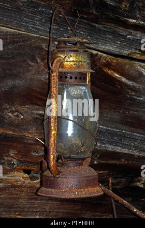 Old, rusty, cold-blast kerosene lantern hanging on the wooden wall of an old barn, awaiting for a new Diogenes to come and find the honest man with it Stock Photo