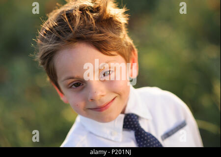 portrait of smiling handsome little kid with fluttering with wind hair in white shirt and tie outdoors nature Stock Photo