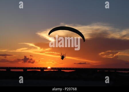 The silhouette of a powered paraglider, paramotor, in front of an orange sky in southern Texas, USA. The sun at dusk with a thundercloud cumulonimbus. Stock Photo