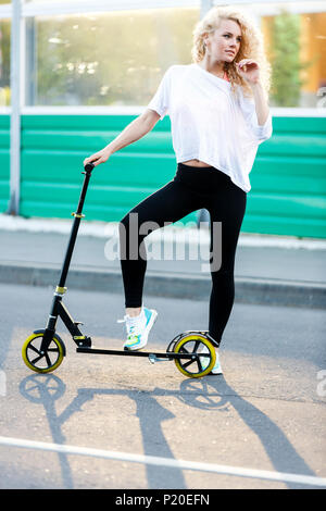 Full-length photo of curly-haired athletic woman kicking on scooter in park Stock Photo