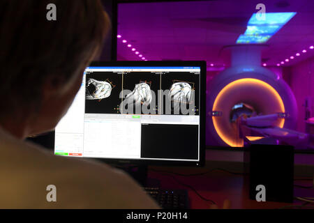 Doctors examining scan on computer with patient on MRI scanner in background Stock Photo