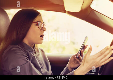 Shocked woman distracted by mobile phone texting while driving a car Stock Photo