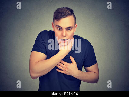 Young man having asthma attack or choking suffering from respiration problems isolated on gray background Stock Photo