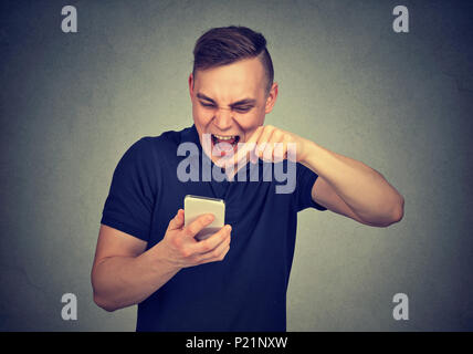 Portrait angry young man screaming on mobile phone isolated on gray wall background. Negative human emotions feelings Stock Photo