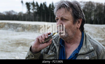 Old man with casual outfit is smoking e-cigarette in forest area Stock Photo