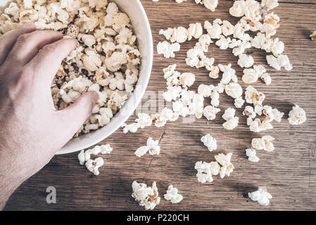 directly above shot of hand grabbing popcorn from bowl on rustic wooden table Stock Photo