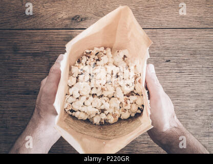 directly above shot of hands holding brown paper bag filled with popcorn Stock Photo