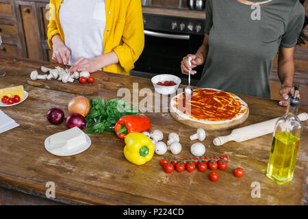 Cropped shot of young women cooking pizza together in kitchen Stock Photo