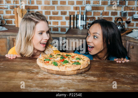 Excited multiethnic women smiling at table with fresh gourmet pizza Stock Photo