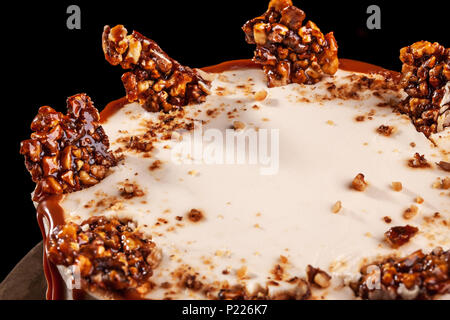 Round white cake with caramel and chocolate puffed rice on a round tray on black background Stock Photo