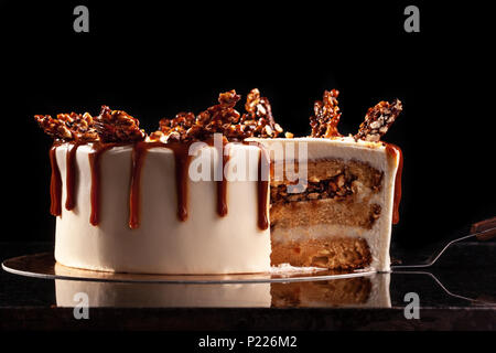 Round white cake with caramel and chocolate puffed rice on a round tray on black background Stock Photo