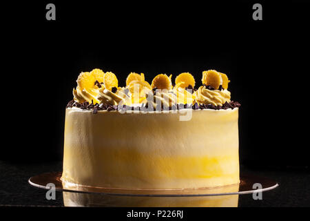 Round yellow birthday cake. Decorative cream decorations on the cake. Black background. Stock Photo