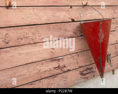 Red fire bucket hanging on the wooden stand, outdoor closeup Stock Photo