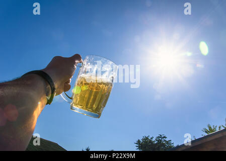 Glass of beer in hand against the background of the sun Stock Photo