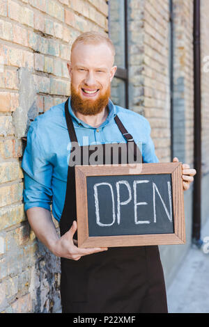 handsome bearded young barista holding sign open and smiling at camera Stock Photo